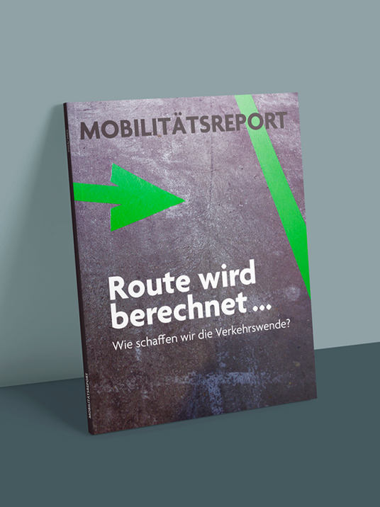 Das Bild zeigt das Cover einer Zeitschrift oder Publikation mit dem Titel "Mobiläts Report" mit einem grünen Pfeil, der nach rechts zeigt. Auf dem Umschlag ist ein Text in deutscher Sprache zu sehen, darunter der Satz "Route wird berechnet..." und die Frage "Wie schaffen wir die Verkehrswende?" Der Text ist in einer Mischung aus Weiß und Schwarz gehalten, wobei der grüne Pfeil und die Frage in Weiß gehalten sind. Das Titelbild steht vor einem dunklen Hintergrund, und das Bild wird als zugänglich für alle Benutzer, einschließlich derjenigen mit Sehbehinderungen, beschrieben.